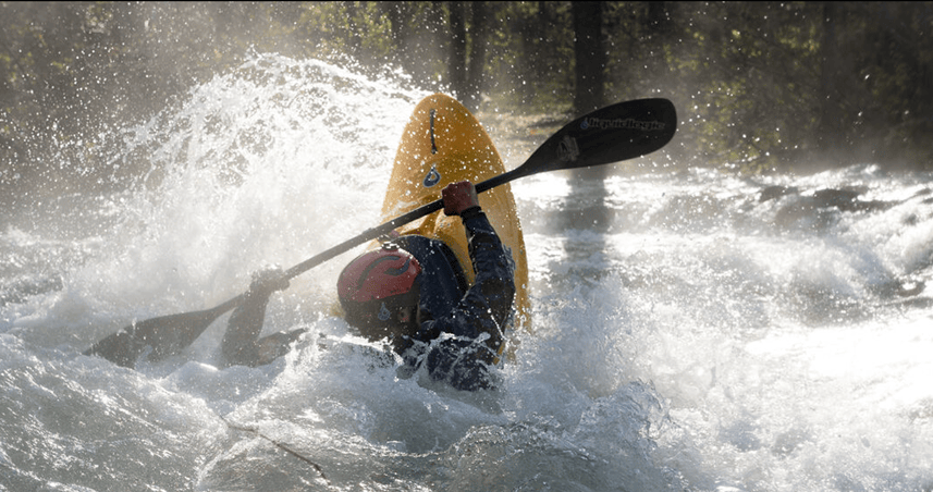 A kayaker throwing a cartwheel in whitewater, spray flying